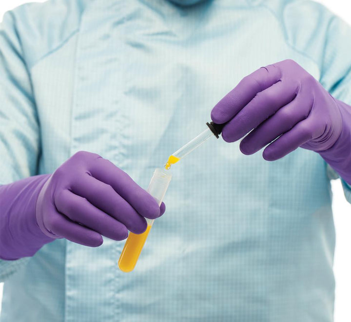 A Person in a Blue Lab Coat Wearing a Pair of Purple BioClean Indigo™ Sterile 300mm Length Nitrile Gloves Dispensing Yellow Liquid from a Pipette into a Conical Vial - Sentinel Laboratories Ltd