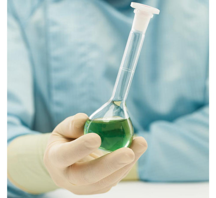 A Person in a Blue Lab Coat wearing White BioClean Legend™ Non-Sterile 300mm Length Latex Gloves Holding a Vial of Green Liquid - Sentinel Laboratories Ltd