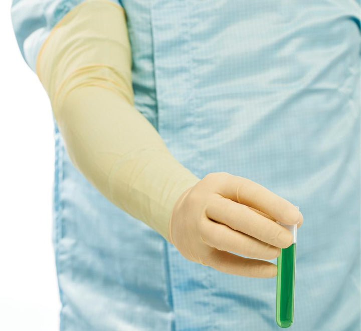 A Person in a Blue Lab Coat Wearing a Single Light Tan Coloured Long Length Cuff BioClean Maxima™ Sterile 600mm Length Latex Glove Holding a Vial of Green Liquid - Sentinel Laboratories Ltd