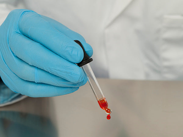 A Person In a White Lab Coat Wearing a Nitritex Omega Techno Nitrile Ambidextrous Blue Glove Squeezing Orange Liquid out of a Pipette