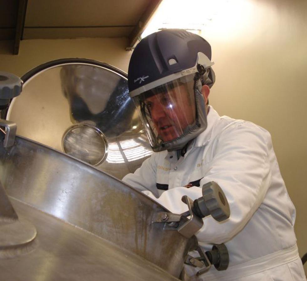 A Man Wearing a Powered Blue PureFlo™ Purelite Xstream Dust Mask in a White Lab Coat looking into a Large Metal Vat - Sentinel Laboratories Ltd