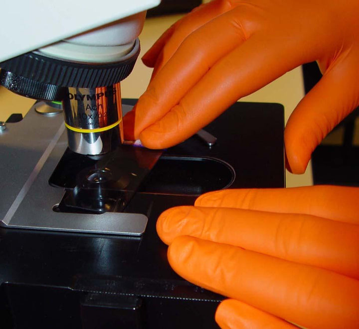 A Person Wearing a Pair of Orange SHIELDskin™ ORANGE NITRILE™ 260 Gloves using a Microscope Close Up - Sentinel Laboratories Ltd