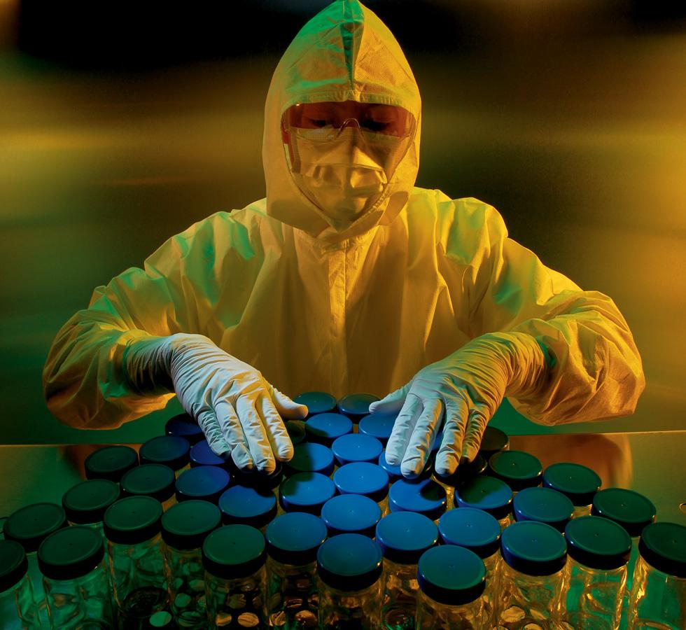 A Person Wearing a White KIMTECH PURE* A5 Sterile Hood, Coverall, Mask and Clear Goggles with their Hands Over a Collection of Conical Tubs with Blue Tops - One Size - Sentinel Laboratories Ltd