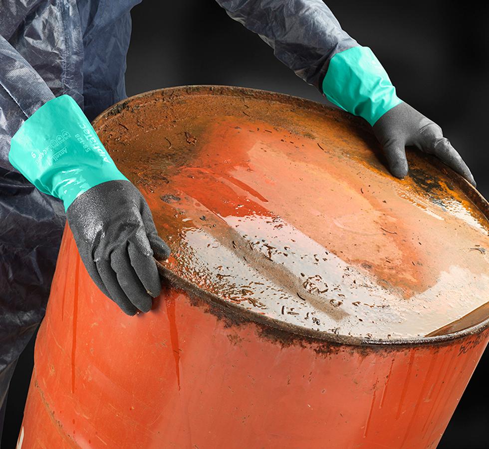 A Person in a Clear Coverall Wearing a Pair of Long Length Cuff ALPHATEC® 58-128 Gloves with Green Coloured Cuffs Holding an Orange Barrel Drum - Sentinel Laboratories Ltd