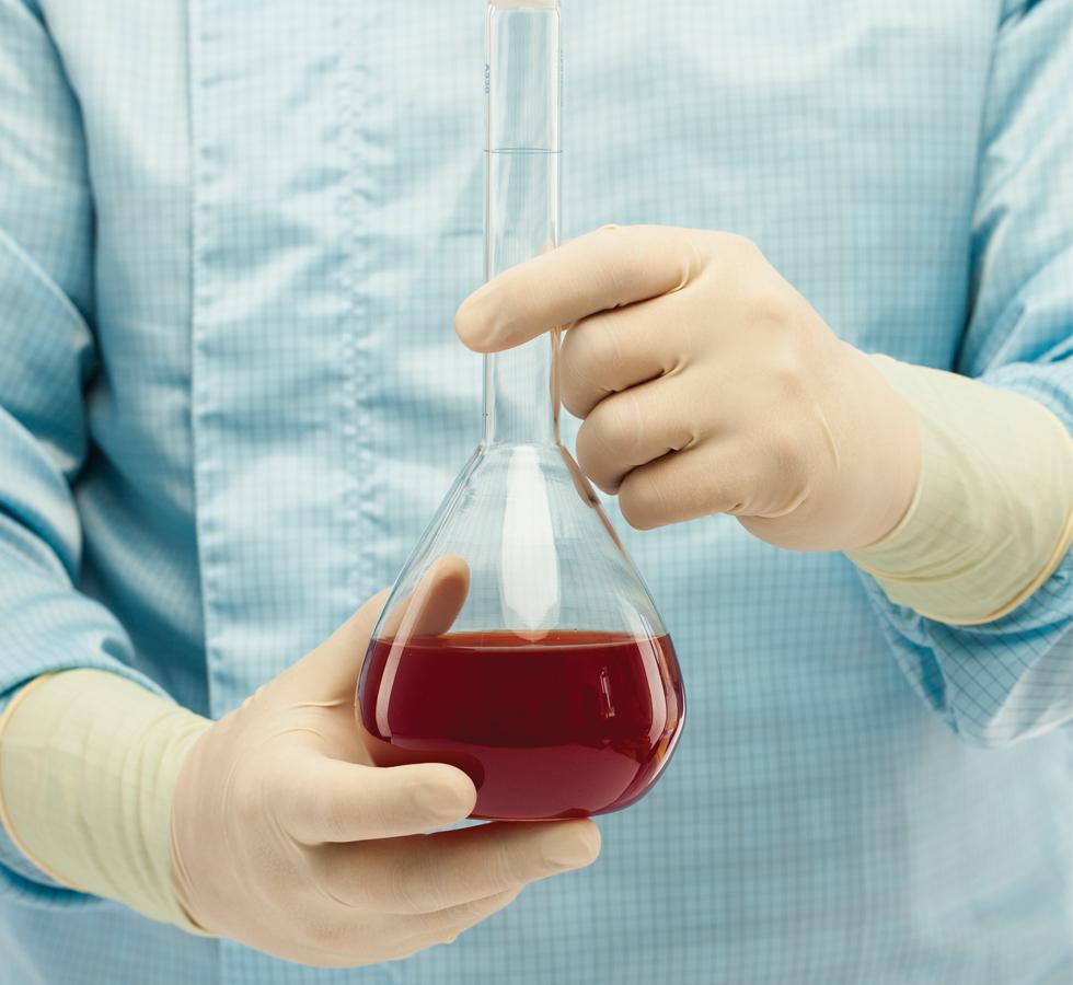 A Person in a Blue Lab Coat Wearing A Pair of Light Tan Coloured BioClean Alpha™ Sterile 300mm Length Latex Gloves Holding a Vial of Red Liquid - Sentinel Laboratories Ltd