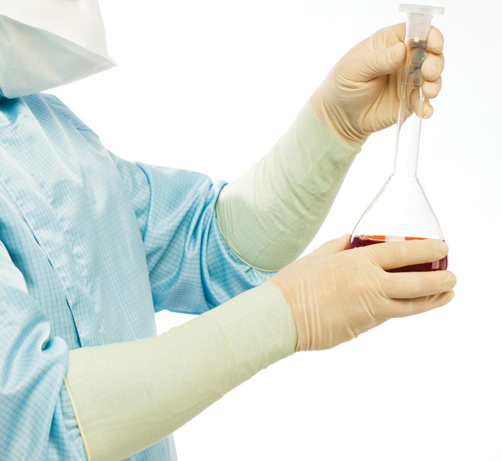 A Person in a Blue Lab Coat Wearing a Pair of Light Tan Coloured Long Length Cuff BioClean Extra™ Sterile 400mm Length Latex Gloves Holding a Vial of Brown Liquid - Sentinel Laboratories Ltd