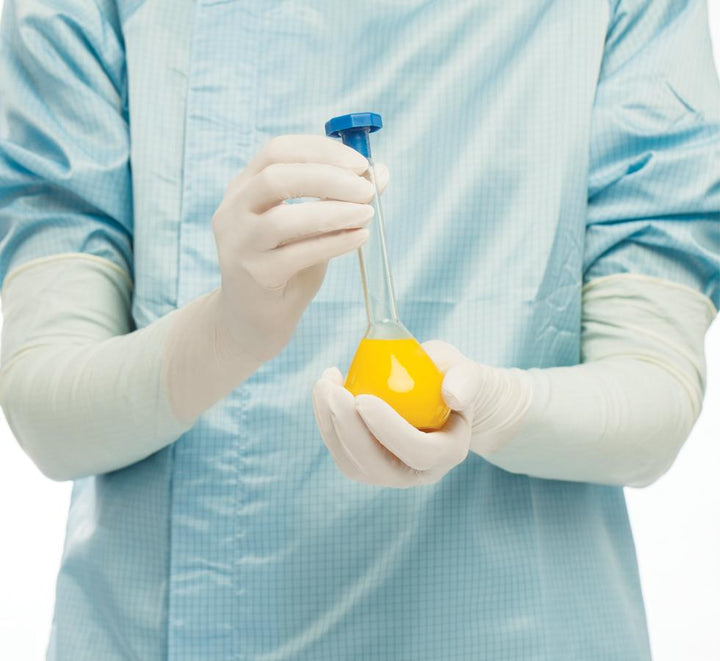 A Person in a Blue Lab Coat Wearing a Pair of White Long Length Cuff BioClean Nitramax™ Sterile 600mm Length Nitrile Gloves Holding a Vial of Yellow Liquid - Sentinel Laboratories Ltd