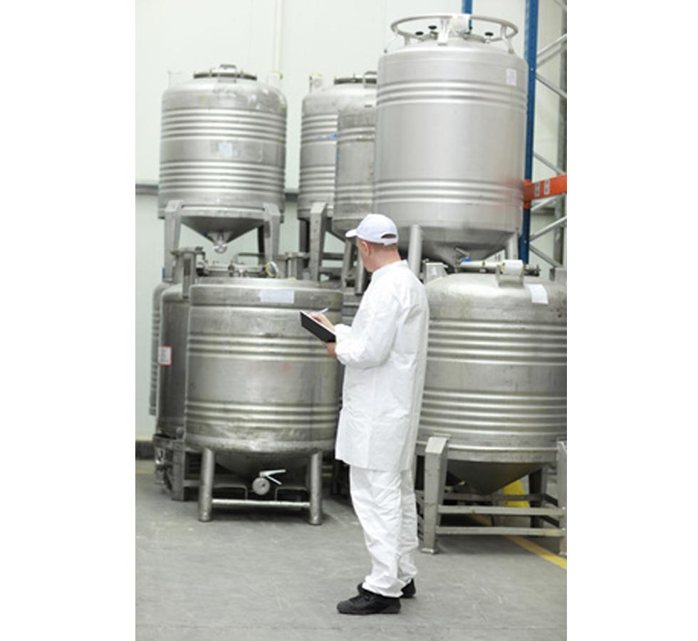 Man writing on a clipboard in front of storing tanks - Food Safety for Manufacturing - Level 1 - Sentinel Laboratories Ltd