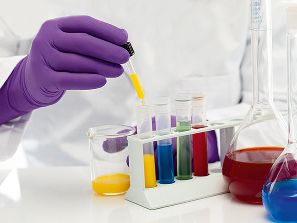 A Person in a White Lab Coat and a Pair of Purple BioClean™ Pro-Tech Nitrile OPT Non Sterile Gloves Filling Multiple Coloured Vials