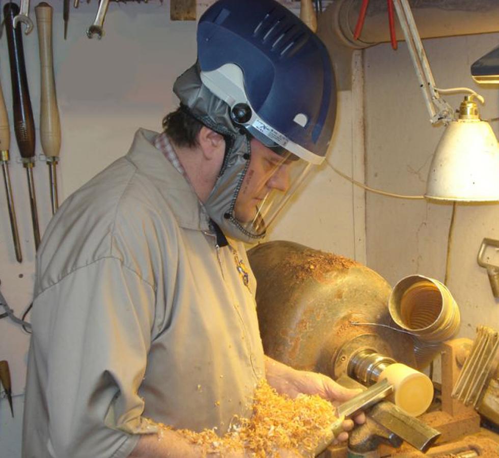 A Man Wearing a Powered Blue PureFlo™ Purelite Xstream Dust Mask in a Tan Jacket doing Woodworking - Sentinel Laboratories Ltd